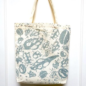 May include: A white canvas tote bag with a blue and white seashell pattern. The bag has two long handles.