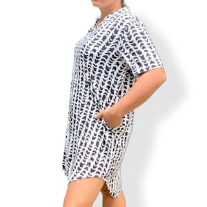 May include: A black and white patterned dress with short sleeves and a collared neckline. The dress features a repeating wave-like design and has pockets. The hemline is slightly asymmetrical. The dress is knee-length.