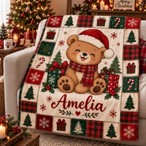May include: A cream-colored throw blanket featuring a central illustration of a brown teddy bear wearing a red Santa hat and a plaid scarf. The bear sits between two gift boxes. The name Amelia is printed in red script below the bear.