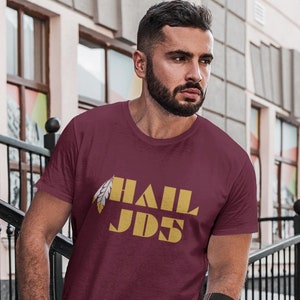May include: A maroon t-shirt with a gold graphic of a feather and the text "HAIL JDS".