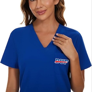 May include: Royal blue V-neck scrub top with a pocket on the left chest. The pocket features the text "DUF" in white with a red stripe underneath. The top has short sleeves.