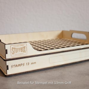 Könnte beinhalten: Ein helles STUFFBOX-Holz-Organizer mit perforierter Oberseite und seitlichen Griffen. Der Text "STAMPS 13 mm" ist auf der Seite sichtbar. Der Organizer ist für die Aufbewahrung konzipiert.