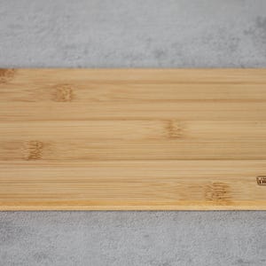 Puede incluir: Una tabla de cortar rectangular de bamb&uacute; marr&oacute;n claro con las palabras "Live Your Dreams" impresas en una peque&ntilde;a etiqueta rectangular en la esquina inferior derecha.