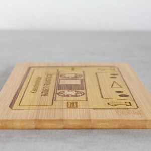 Puede incluir: Una tabla de cortar de madera con un dise&ntilde;o de cinta de casete. El texto "TAUGHT FROM THE HEART" y "Kassenbon" est&aacute; grabado en la tabla.