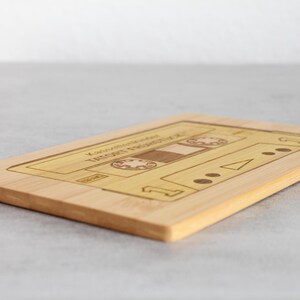 Puede incluir: Una tabla de cortar de madera con forma de casete con el texto "You Are My Favorite Thing That I Got For Free" grabado en ella.