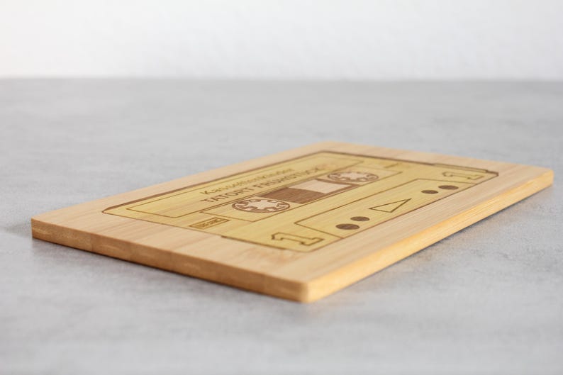 Puede incluir: Una tabla de cortar de madera con forma de casete con el texto "You Are My Favorite Thing That I Got For Free" grabado en ella.