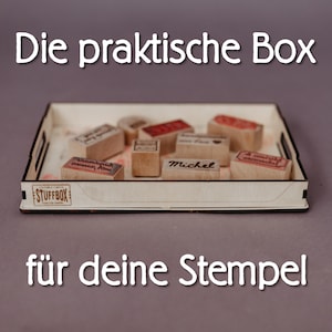 Könnte beinhalten: Ein rechteckiges Tablett aus hellem Holz, das mehrere kleine Holzstempel mit verschiedenen Stempelabdrücken enthält. Auf der Vorderseite des Tabletts befindet sich ein Logo mit dem Text STUFFBOX. Das Bild enthält den Text Die praktische Box für deine Stempel.
