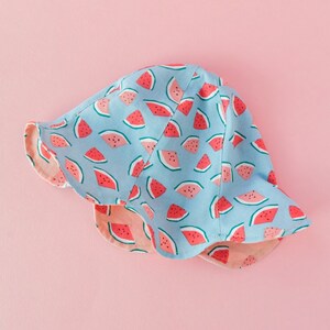 May include: A blue and pink sun hat with a watermelon print. The hat has a wide brim and a ruffled edge.