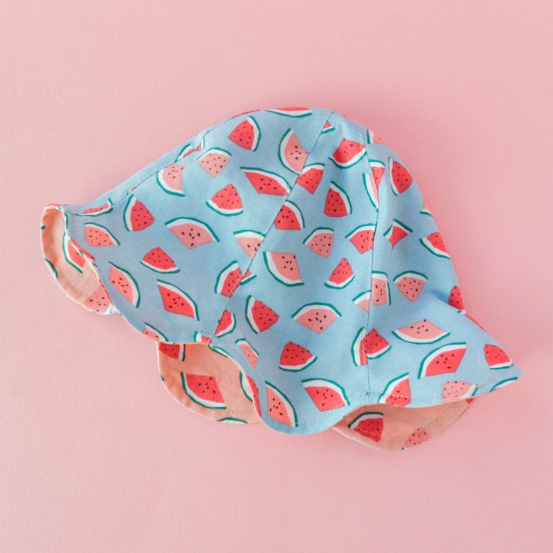 May include: A blue and pink sun hat with a watermelon print. The hat has a wide brim and a ruffled edge.