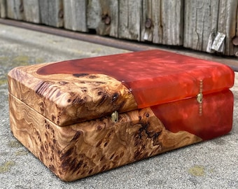Op de afbeelding: Een houten doos met een rode harsinleg. De doos heeft een scharnierend deksel en is gemaakt van natuurlijk hout met een uniek houtnerfpatroon.