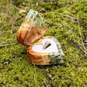 May include: A heart-shaped wooden ring box with a green and white resin inlay. The box is open and a diamond ring is inside.