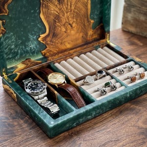 May include: A wooden jewelry box with a green resin exterior and a natural wood grain lid. Inside, it holds two watches, rings, and cufflinks. The watches have leather and stainless steel bands. The box is open, revealing the contents.