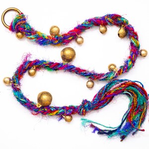 May include: A colorful braided cord with a tassel and gold-toned bells. The cord is made of multiple strands of yarn in shades of pink, blue, green, red, and purple.