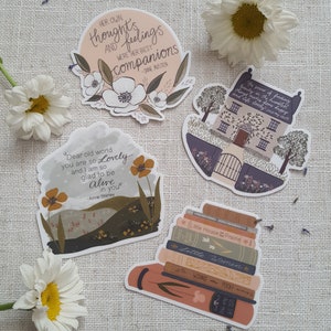 May include: Five illustrated stickers featuring quotes from classic literature. The stickers are on a white fabric background. The quotes are: "Her own thoughts and feelings were her best companions - Jane Austen", "Dear old world you are so lovely and I am so glad to be alive in you - Anne Shirley", "The power of finding beauty in the humblest things makes home happy and life lovely", "Little House on the Prairie", "Little Women".