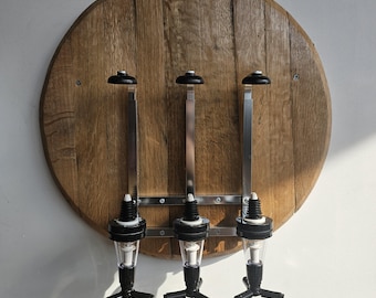 May include: A wooden wall-mounted liquor dispenser with three black and silver liquor pourers. The dispenser is made from a round piece of wood with a natural wood grain.