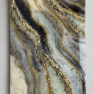 May include: A rectangular wall art piece featuring a glossy resin finish with swirling patterns of black, white, and gray. The design is accented by textured gold glitter lines and embedded clear glass crystals that create a geode-like appearance.