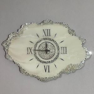 Può includere: Un orologio da parete dalla forma irregolare a geode con un quadrante in resina marmorizzata bianco crema. L'orologio presenta numeri romani argentati alle posizioni delle dodici, tre, sei e nove, bordato da vetro a specchio argentato.