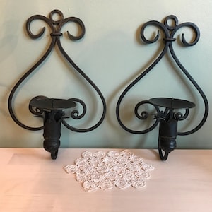 May include: A pair of black metal wall sconces with a scrolled design. Each sconce has a candle holder with a round base and a decorative finial.