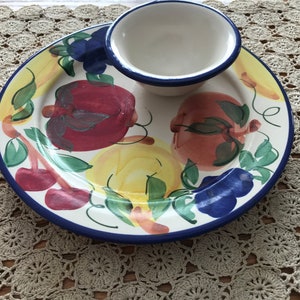May include: A white ceramic serving dish with a blue rim and a small white bowl with a blue rim. The dish is decorated with a colorful fruit design, including red, yellow, and green fruits.