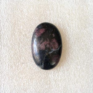 Puede incluir: Gema de forma ovalada con superficie pulida. La piedra es principalmente negra con parches irregulares de rojo intenso y toques de blanco. La gema probablemente se utiliza para joyer&iacute;a o fines decorativos.