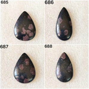 May include: Four teardrop-shaped gemstones with a dark, speckled appearance. Each stone has a polished surface with a mix of dark and lighter colors, including a deep black and reddish-purple. The gemstones are numbered 685, 686, 687, and 688.