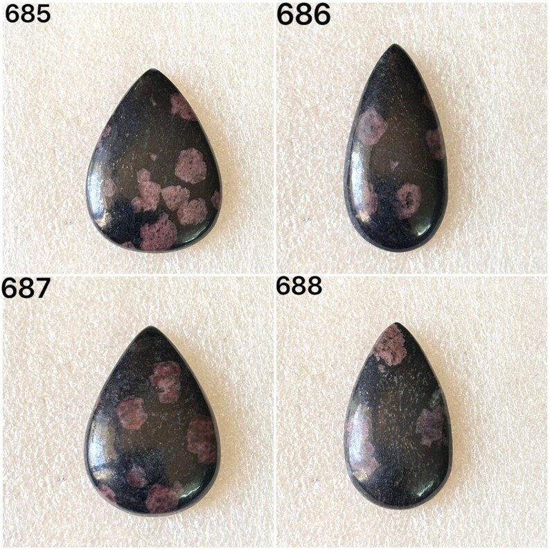 Puede incluir: Cuatro piedras preciosas en forma de l&aacute;grima con un aspecto oscuro y moteado. Cada piedra tiene una superficie pulida con una mezcla de colores oscuros y claros, incluyendo un negro profundo y un p&uacute;rpura rojizo. Las piedras preciosas est&aacute;n numeradas 685, 686, 687 y 688.