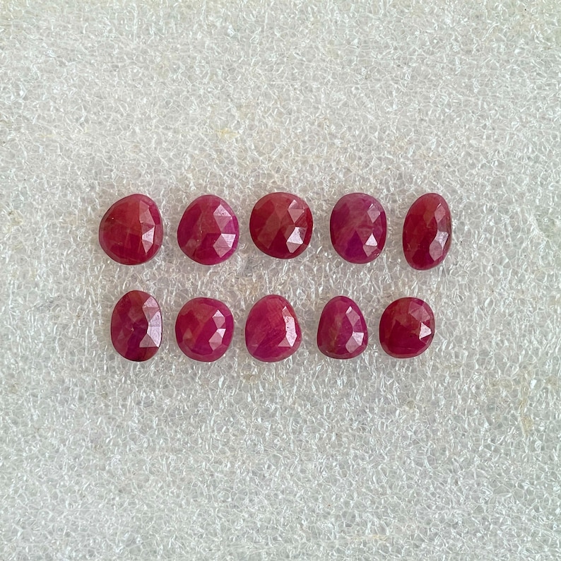 Puede incluir: Diez rub&iacute;es peque&ntilde;os, facetados y de forma ovalada dispuestos en dos filas horizontales de cinco. Cada piedra preciosa muestra un color rojo intenso y saturado con una superficie pulida y multifacetada que refleja la luz, creando un brillo.