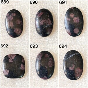 Könnte beinhalten: Sechs polierte Edelsteine mit dunklem Hintergrund und unterschiedlichen Formen. Jeder Stein hat eine Mischung aus dunklen und hellvioletten Einschlüssen. Die Edelsteine sind mit 689, 690, 691, 692, 693 und 694 nummeriert.