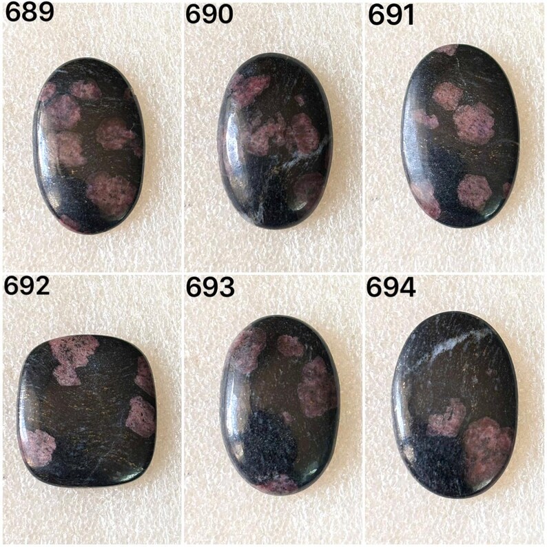 Puede incluir: Seis piedras preciosas pulidas con fondo oscuro y formas variadas. Cada piedra tiene una mezcla de inclusiones moradas oscuras y claras. Las piedras preciosas est&aacute;n numeradas 689, 690, 691, 692, 693 y 694.