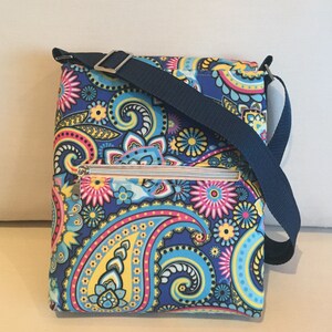 May include: A rectangular crossbody bag with a vibrant paisley pattern in shades of blue, pink, yellow, and turquoise. The bag features a navy blue adjustable strap and a silver zipper. The bag is designed for everyday use.