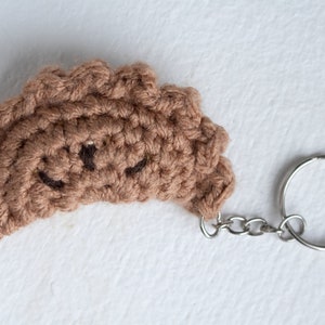 May include: A brown crocheted empanada keychain with a silver chain and ring.