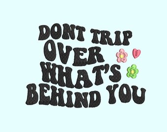 May include: Black embroidered text on a light blue background that reads "Don't trip over what's behind you". There are two pink and green flowers and a pink heart to the right of the text.