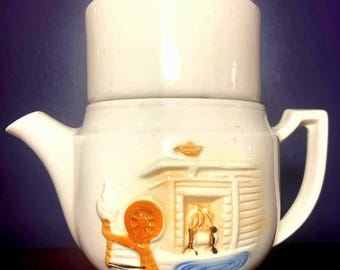May include: White ceramic coffee pot with a lid and a handle. The pot has a scene of a cabin with a fireplace and a person in front of it. The scene is painted in orange, brown, and blue.