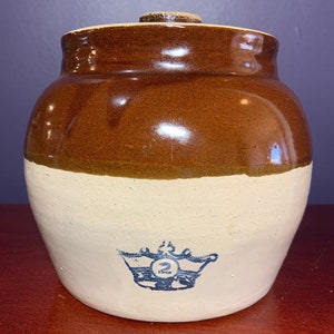 May include: A brown and white glazed ceramic crock with a lid. The crock has a blue and white crown with the number "2" inside the crown.
