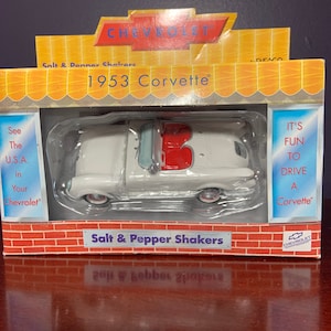 May include: A white 1953 Chevrolet Corvette salt and pepper shaker set. The car is a miniature replica of the classic sports car. The packaging features a brick wall background and the text "See The U.S.A. in Your Chevrolet".