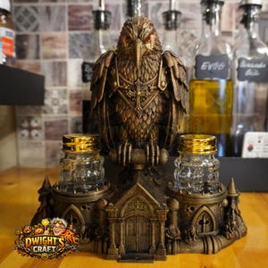 May include: A bronze-colored eagle figurine perched atop a gothic-style structure with two clear glass salt and pepper shakers featuring gold-tone lids. The base includes architectural details like arched doorways and small towers.