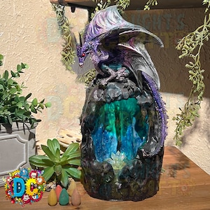 以下が含まれることがあります： 黒と緑の山をデザインした紫色のドラゴン香炉。ドラゴンは山の頂上に止まっており、虹色の翼を持っている。山には緑と青の光が輝いている