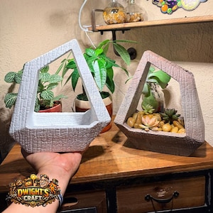 May include: Two geometric, angular planters with a textured, stone-like finish. One planter is white, and the other is a muted brown. The brown planter contains small succulents and smooth pebbles. Both have an open, asymmetrical frame design.