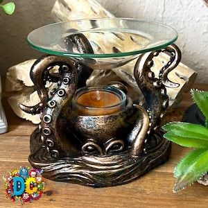 May include: A bronze octopus-shaped oil burner with a glass dish on top. The octopus has a detailed design with tentacles and suckers. A small tea light candle sits in the center of the burner.
