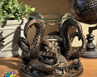 May include: Bronze-colored octopus-themed oil warmer with a glass dish and a candle holder. The tentacles form the base, with a treasure chest detail. A small plant and a globe are in the background.