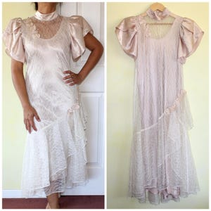 May include: A vintage blush-colored lace dress with a satin bodice and puffed sleeves. The dress has a high neckline and a layered skirt.