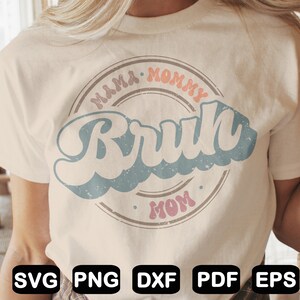 Puede incluir: Una camiseta beige claro con un dise&ntilde;o gr&aacute;fico de estilo retro. El gr&aacute;fico presenta un c&iacute;rculo con el texto "Mama Mommy Mom" y la palabra "Bruh" en una fuente grande de color azul.