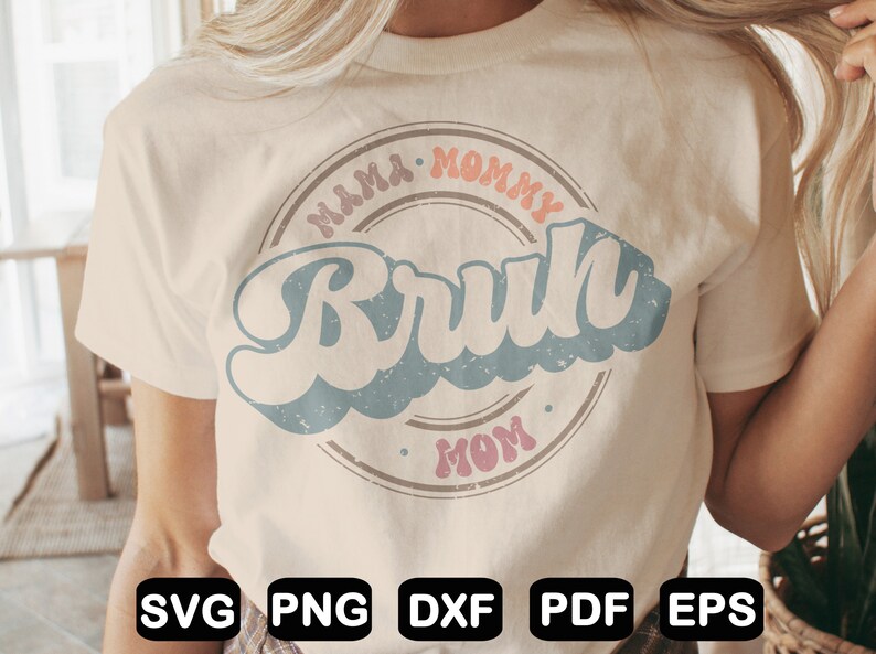 Puede incluir: Una camiseta beige claro con un dise&ntilde;o gr&aacute;fico de estilo retro. El gr&aacute;fico presenta un c&iacute;rculo con el texto "Mama Mommy Mom" y la palabra "Bruh" en una fuente grande de color azul.