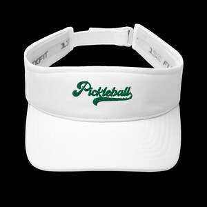 K&ouml;nnte beinhalten: Wei&szlig;es Visier mit dem Wort "Pickleball" in gr&uuml;ner Schrift auf der Vorderseite gestickt. Das Visier hat einen gebogenen Schirm und einen verstellbaren Riemen. Die Marke Flexfit ist auf der Seite sichtbar.