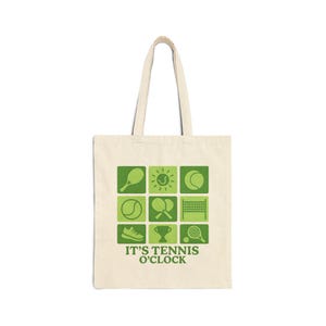May include: Cream-colored tote bag with green tennis-themed graphics. The design includes tennis balls, rackets, and a net, arranged in a grid. The text "IT'S TENNIS O'CLOCK" is printed below the graphics. The bag has two handles.