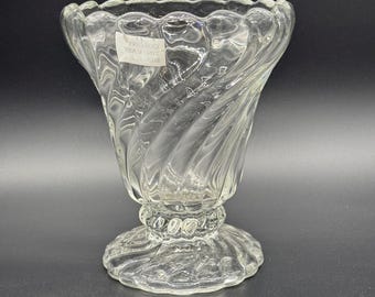 May include: A clear glass vase with a swirl design and a scalloped rim. The vase has a pedestal base with a beaded trim.