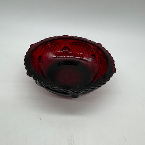 May include: A small, red glass bowl with a scalloped edge and a decorative pattern. The bowl is made of ruby red glass and has a clear, shiny finish.