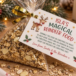 May include: A clear plastic bag filled with oat-based reindeer food, tied with a gold ribbon and a white rectangular tag. The tag features a reindeer illustration, a North Pole sign, holly, and text reading ISLA'S MAGICAL REINDEER FOOD.