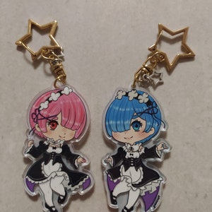 Op de afbeelding: Twee anime-personage sleutelhangers met Rem en Ram uit de anime Re:Zero. De sleutelhangers zijn gemaakt van helder acryl en tonen de personages in hun dienstmeidenoutfits. Rem heeft blauw haar en blauwe ogen, terwijl Ram roze haar en rode ogen heeft. Beide sleutelhangers hebben een gouden ster-hanger.