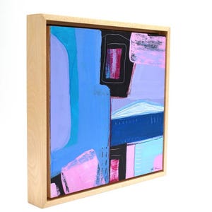 May include: Abstract painting in a natural wood frame. The artwork features a composition of blue, purple, pink, and black shapes. The painting has a modern aesthetic, with a mix of geometric and organic forms. The frame is a light, natural wood color.